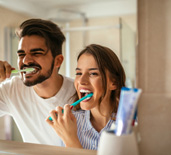 Couple smiling while brushing teeth in bathroom